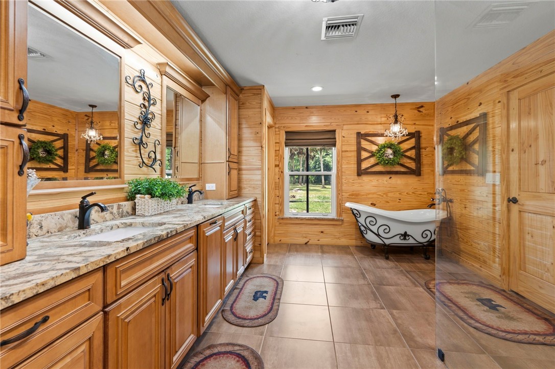 Natural wood paneling throughout, dual vanity with granite countertops, wood-finish flooring, a freestanding clawfoot bathtub, and an exterior-facing window