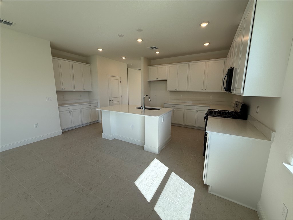 Spacious kitchen with a central island, recessed lighting, white cabinetry, integrated sink, and tile flooring