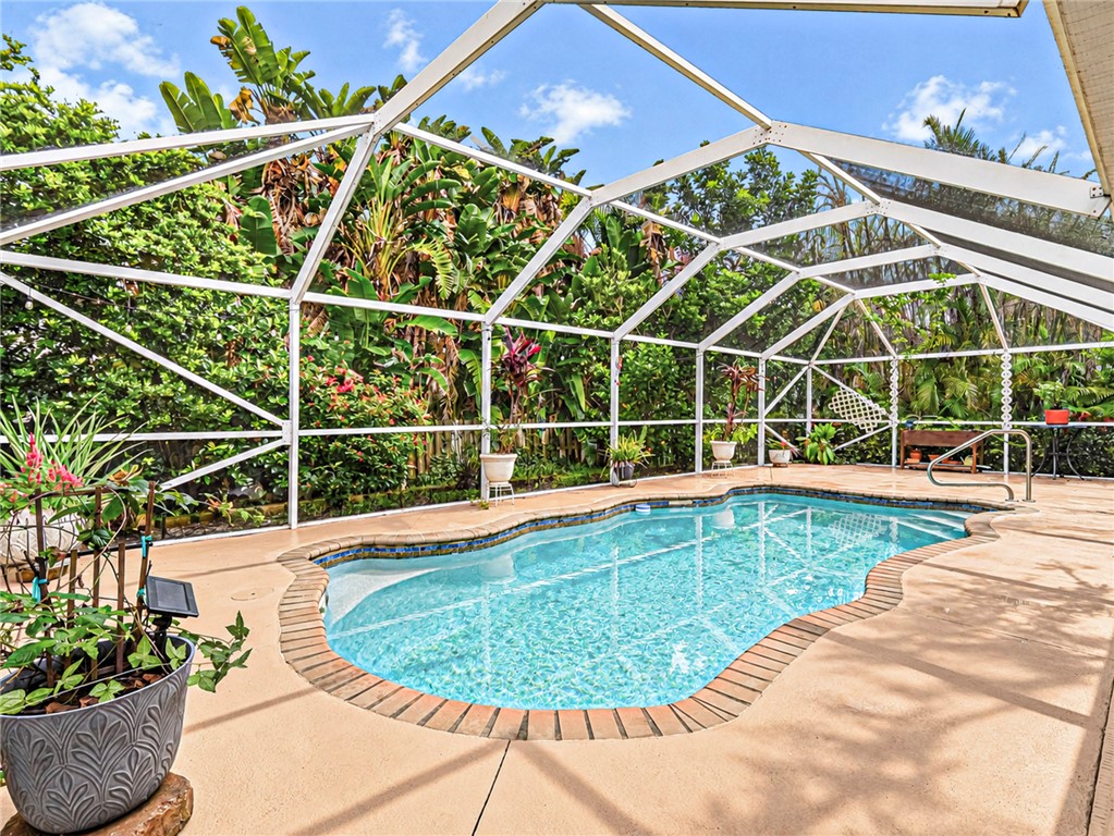 Screened pool enclosure featuring a freeform swimming pool with brick coping, concrete decking, and lush landscaping