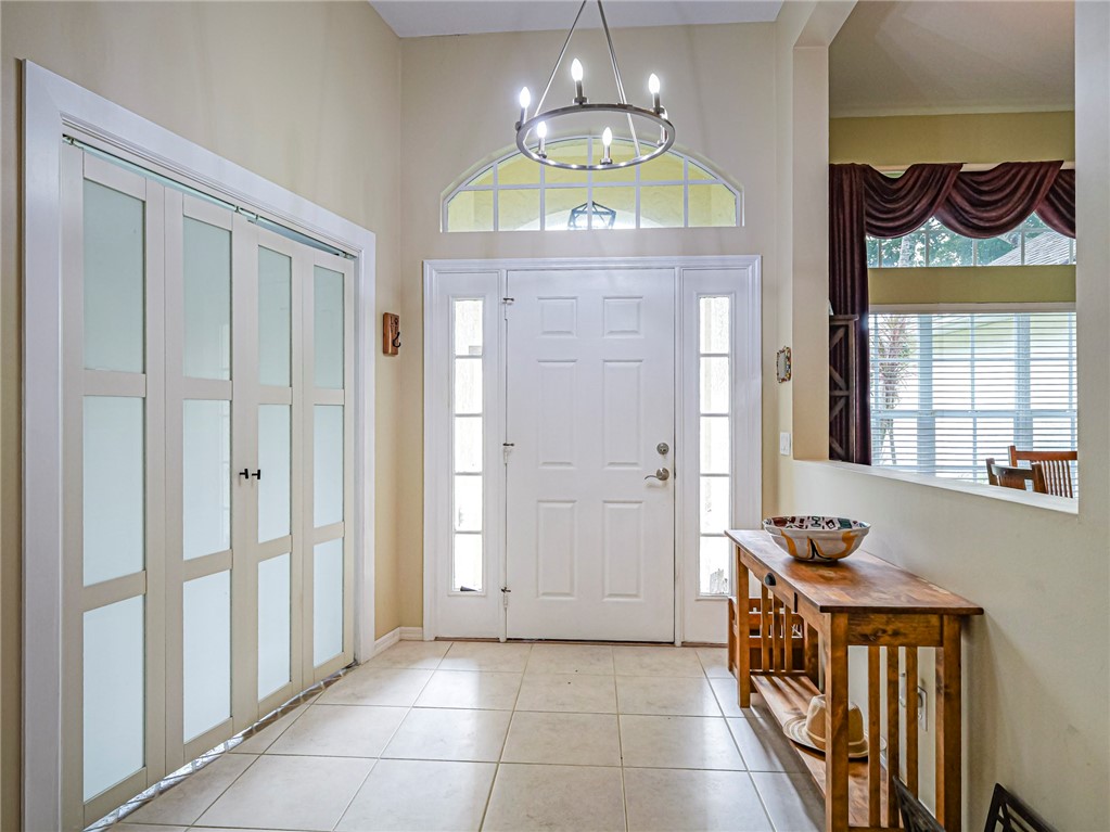 Entryway featuring a double-paneled front door with side lites, an arched transom window, a rectangular chandelier, and neutral-toned tile flooring