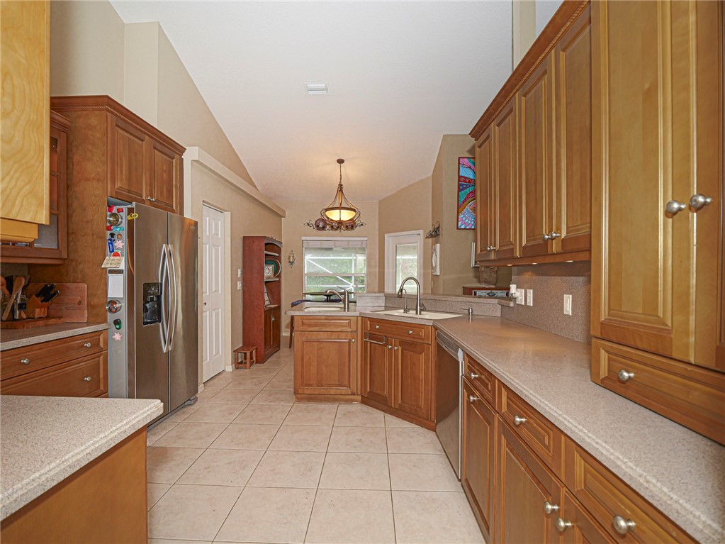 Kitchen featuring wood-finish cabinetry, solid surface countertops, a stainless steel side-by-side refrigerator, tile flooring, and a vaulted ceiling