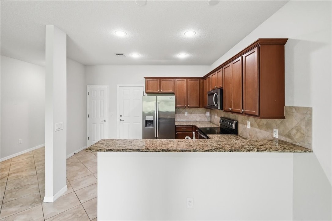 Kitchen featuring wood cabinetry, stainless steel appliances, a tiled backsplash, and stone countertops, including a breakfast bar