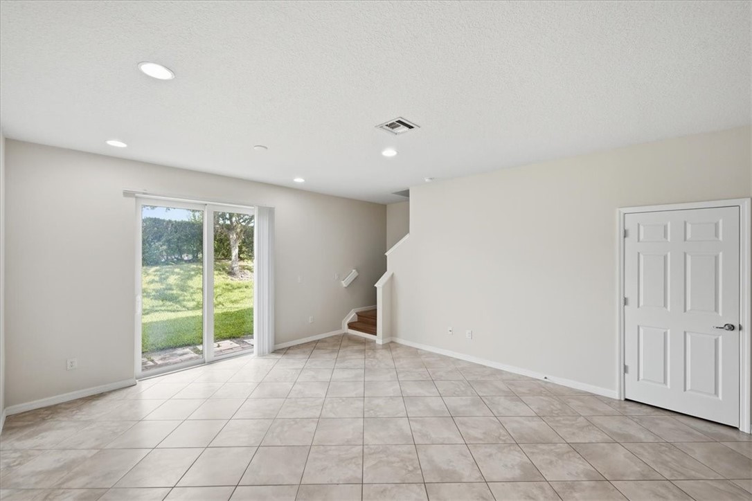 Spacious living area featuring neutral-toned tile flooring, recessed ceiling lighting, and a white six-panel door