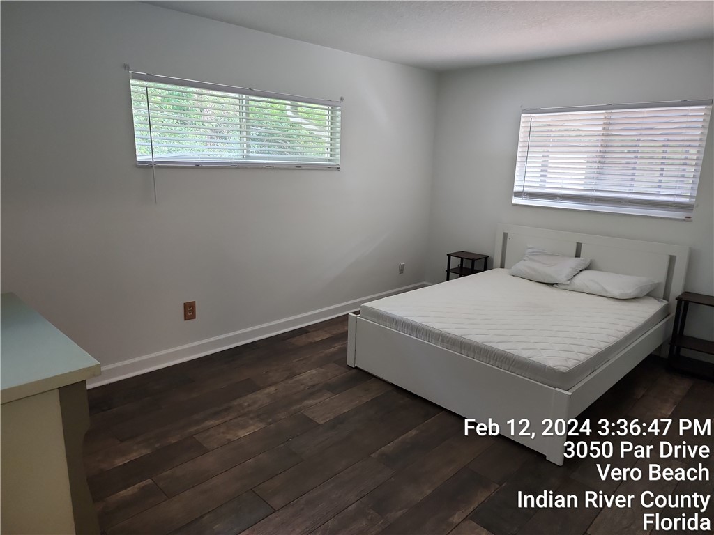 Wood-finish flooring with white baseboards, white walls, and horizontal window blinds