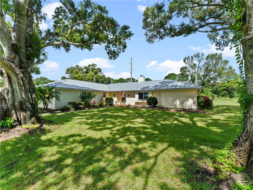 Expansive front lawn with mature trees, a light-colored exterior, and a metal roof