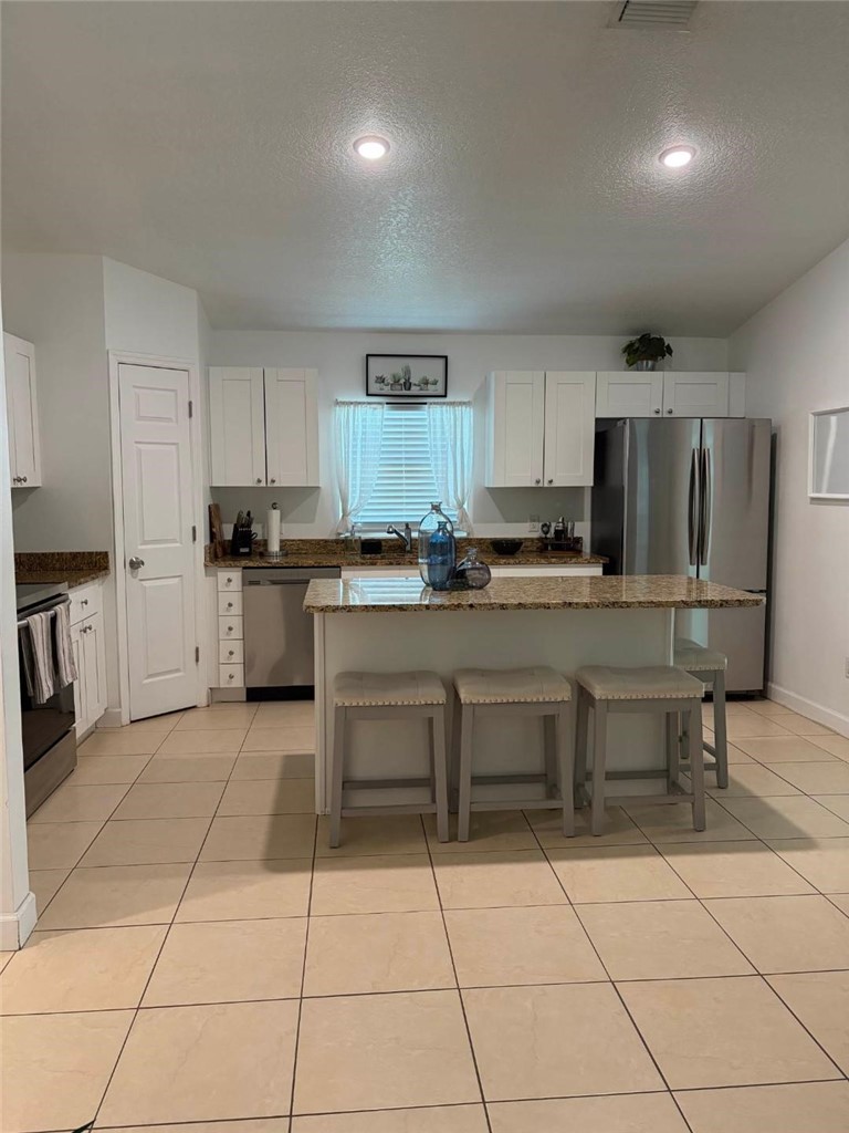 Kitchen featuring an island with stone countertop, white cabinetry, stainless steel appliances, and tile flooring