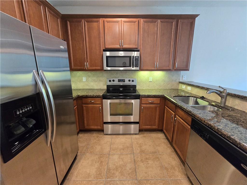Full kitchen with stainless steel appliances, wood cabinetry, granite-finish countertops, and tiled flooring