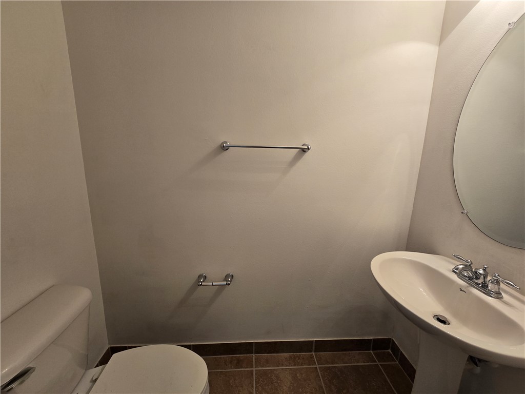 Pedestal sink with chrome faucet, oval mirror, and large format tile flooring