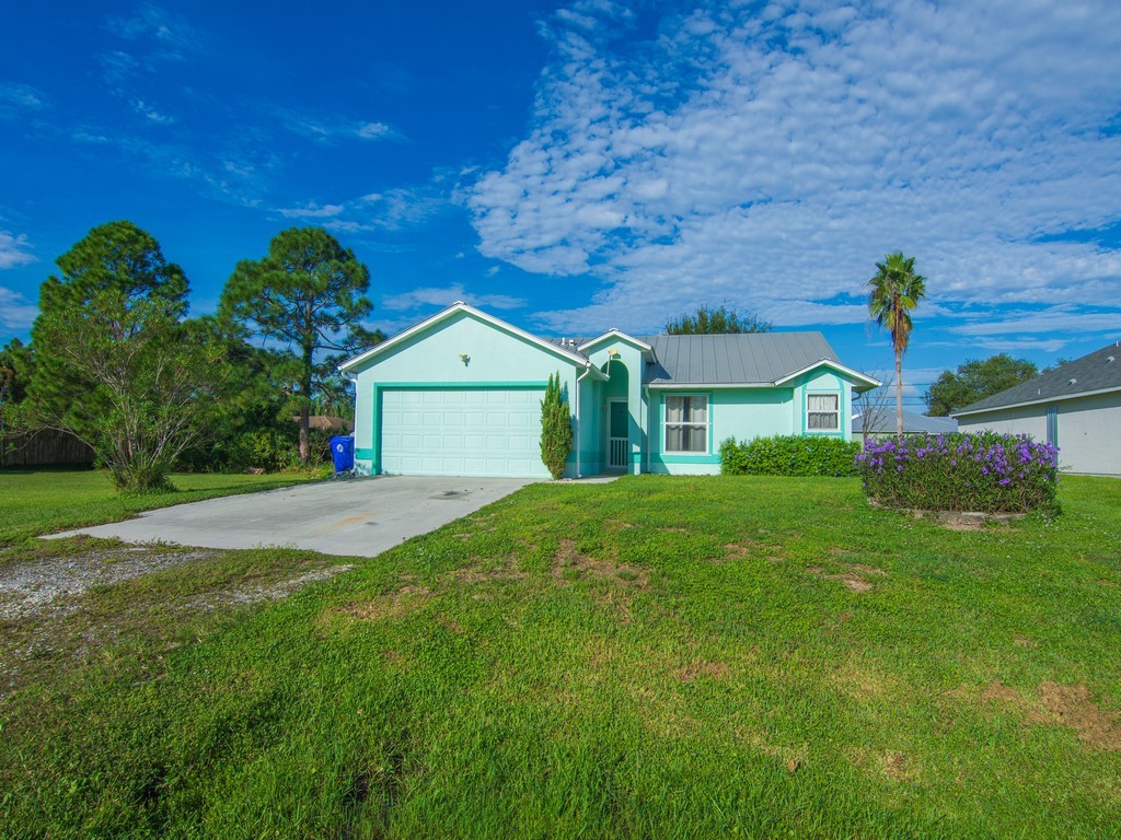 Mint green exterior with an attached garage, a concrete driveway, and a manicured lawn