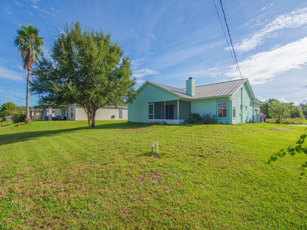 Expansive green lawn surrounds a pale green residence with a metal roof and screened patio