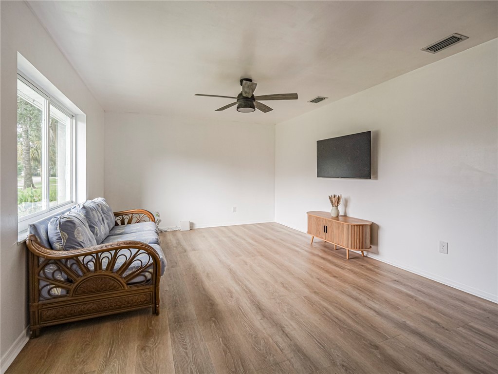 Spacious room featuring wood-finish flooring, a ceiling fan, and large windows