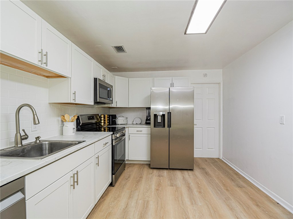 White cabinetry with brushed nickel hardware, stainless steel appliances, wood-finish flooring, white subway tile backsplash, and light-toned countertops
