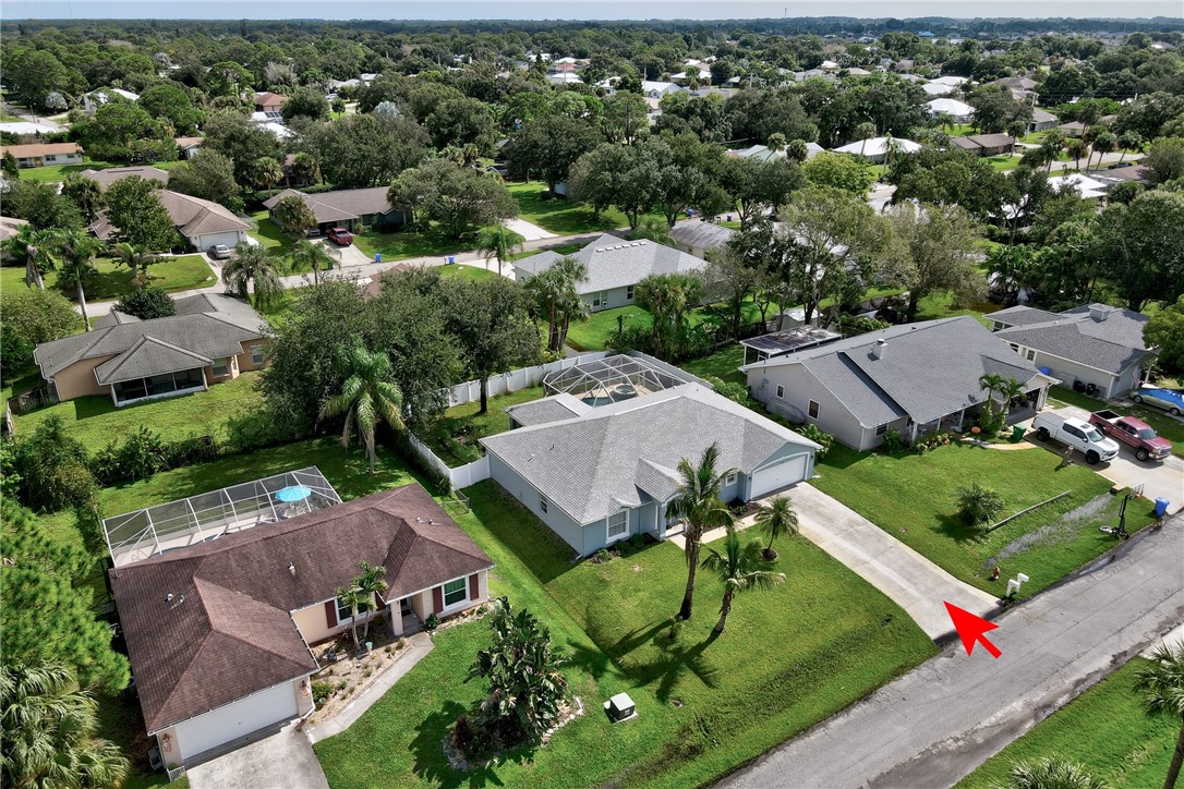 Aerial view showcasing this residential property featuring a modern white roof structure on expansive manicured grounds, mature landscaping with palm trees, and a generously proportioned lot surrounded by established neighborhood properties with lush green space