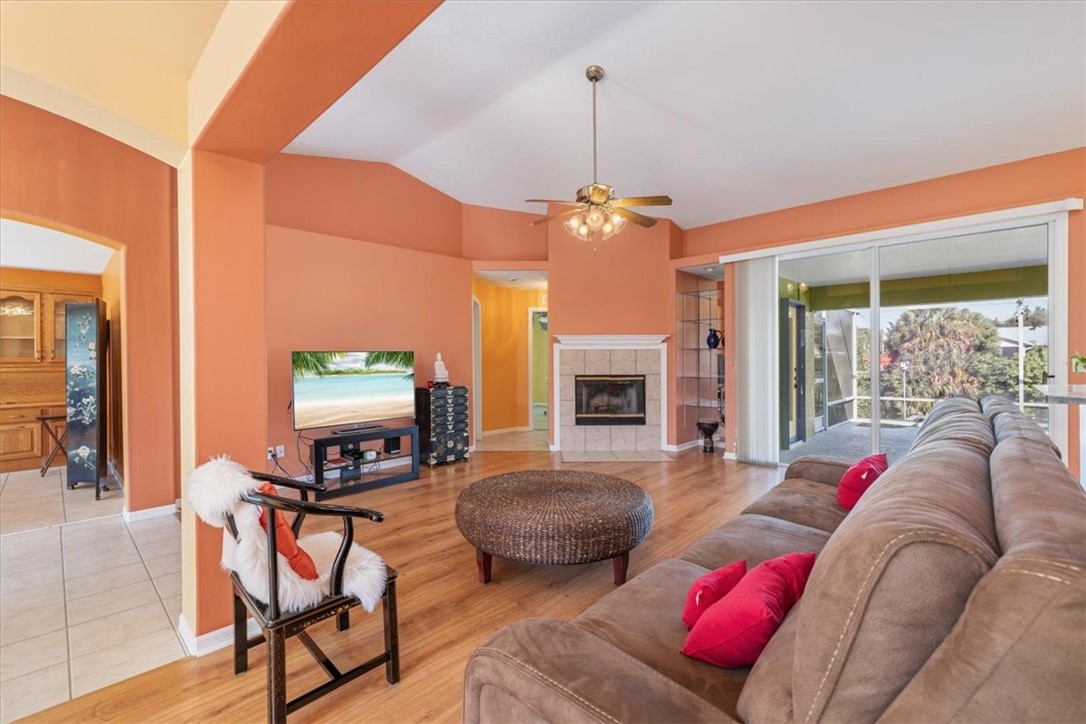 Vaulted ceiling with a ceiling fan, wood-finish flooring, corner fireplace with a tiled surround, and expansive sliding glass doors
