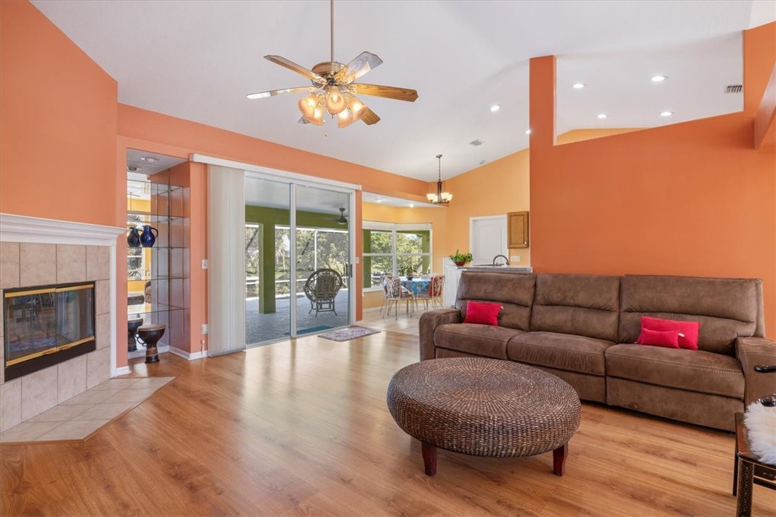 Vaulted ceilings, wood-finish flooring, tiled fireplace, glass sliding doors, and a ceiling fan with integrated lighting