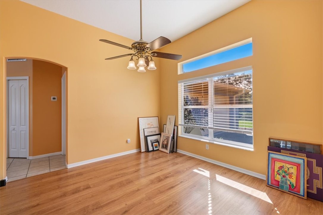 Vaulted ceiling with a ceiling fan light fixture, wood-finish flooring, transom window, and a window with blinds