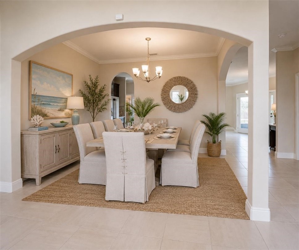 Arched entryway leading to a dining space featuring crown molding, a multi-light chandelier, and light-toned tile flooring