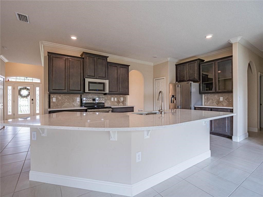 Kitchen featuring arched walkways, dark brown cabinetry, backsplash, crown molding, and light tile patterned flooring
