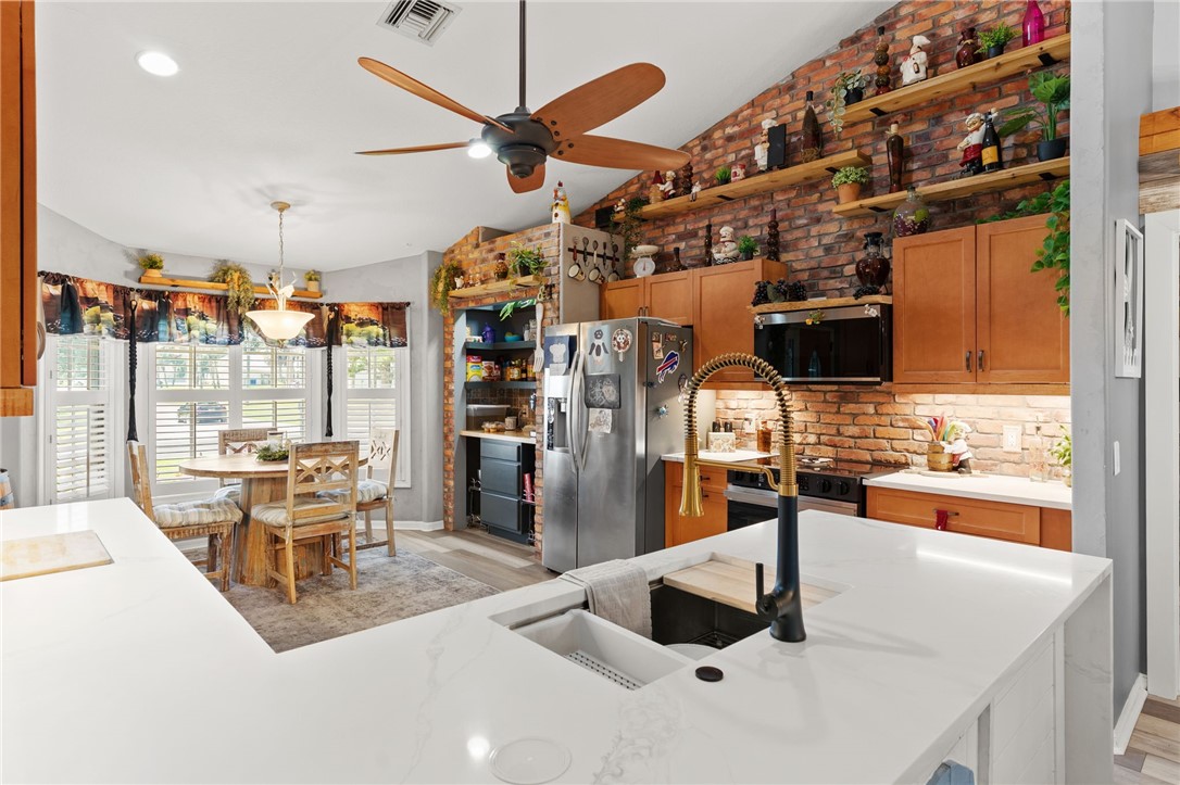 Kitchen featuring white countertops, brick backsplash, wood-finish cabinetry, and an integrated stainless steel sink with a matte black and gold-finish faucet