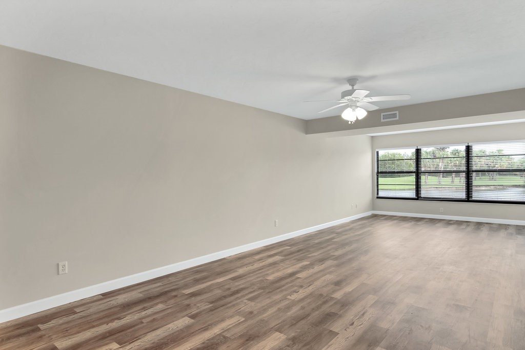 Spacious room featuring wood-finish flooring, light-toned walls, a ceiling fan, and large windows