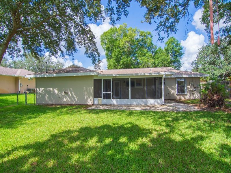 Expansive backyard featuring a manicured lawn, screened patio, and mature trees