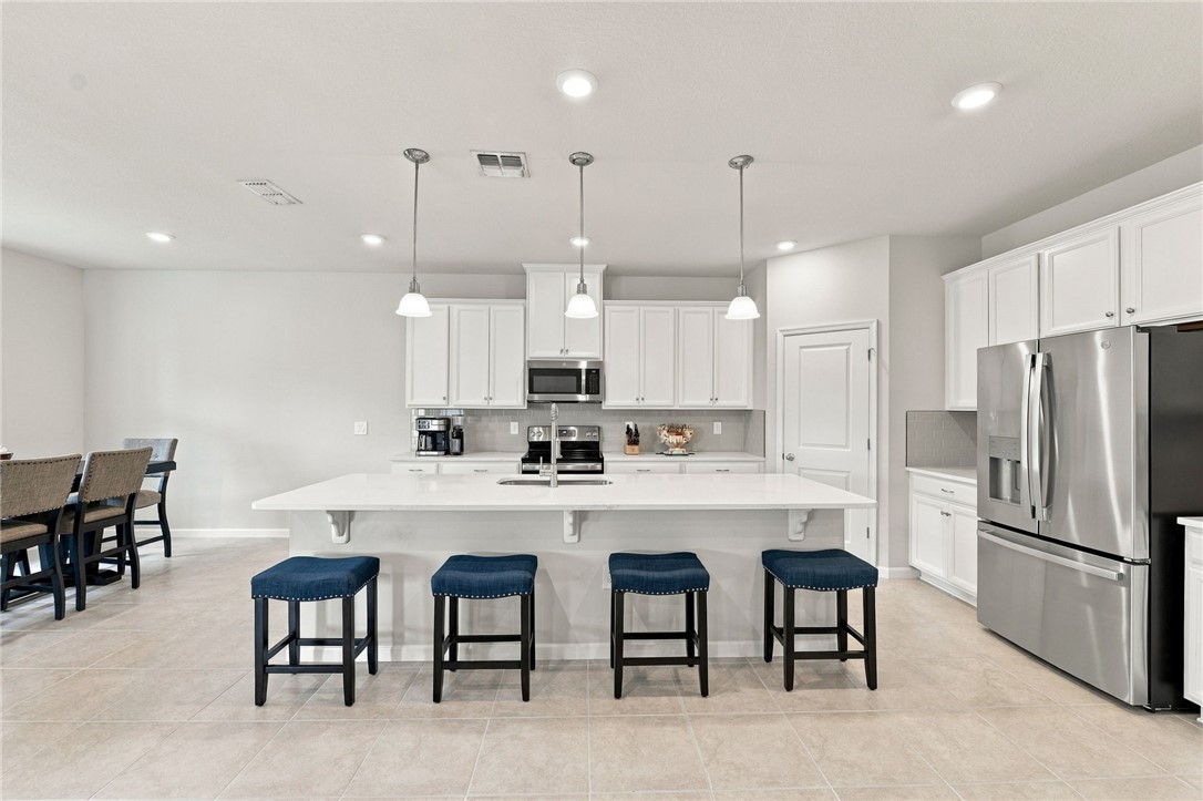 Spacious kitchen featuring white cabinetry, a large center island, stainless steel appliances, a tile backsplash, and recessed lighting