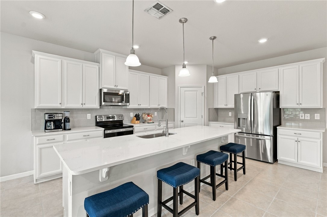 Kitchen featuring white cabinetry, stainless steel appliances, a center island with sink, pendant lighting, and tiled flooring