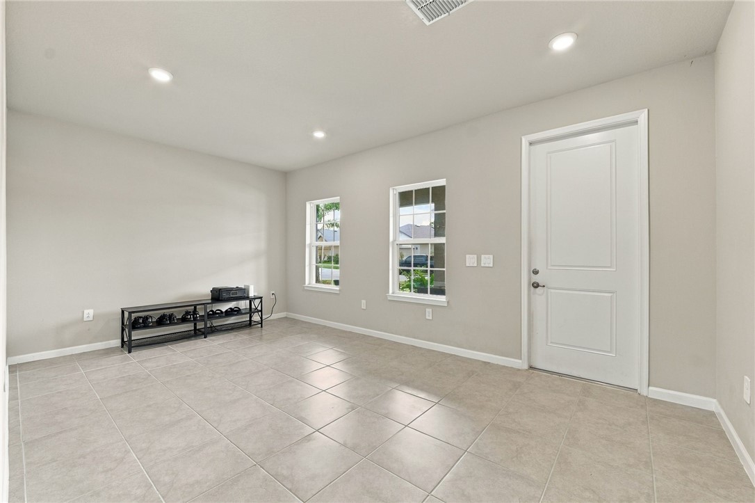 Recessed lighting, light gray walls, white trim, two pane windows, and light neutral tile flooring
