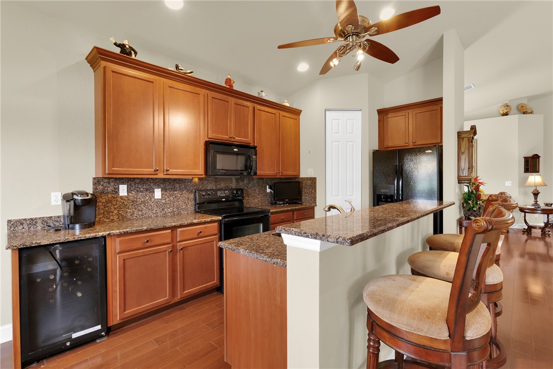 Kitchen featuring wood-finish flooring, wood cabinetry, stone countertops, and a breakfast bar and beverage cooler