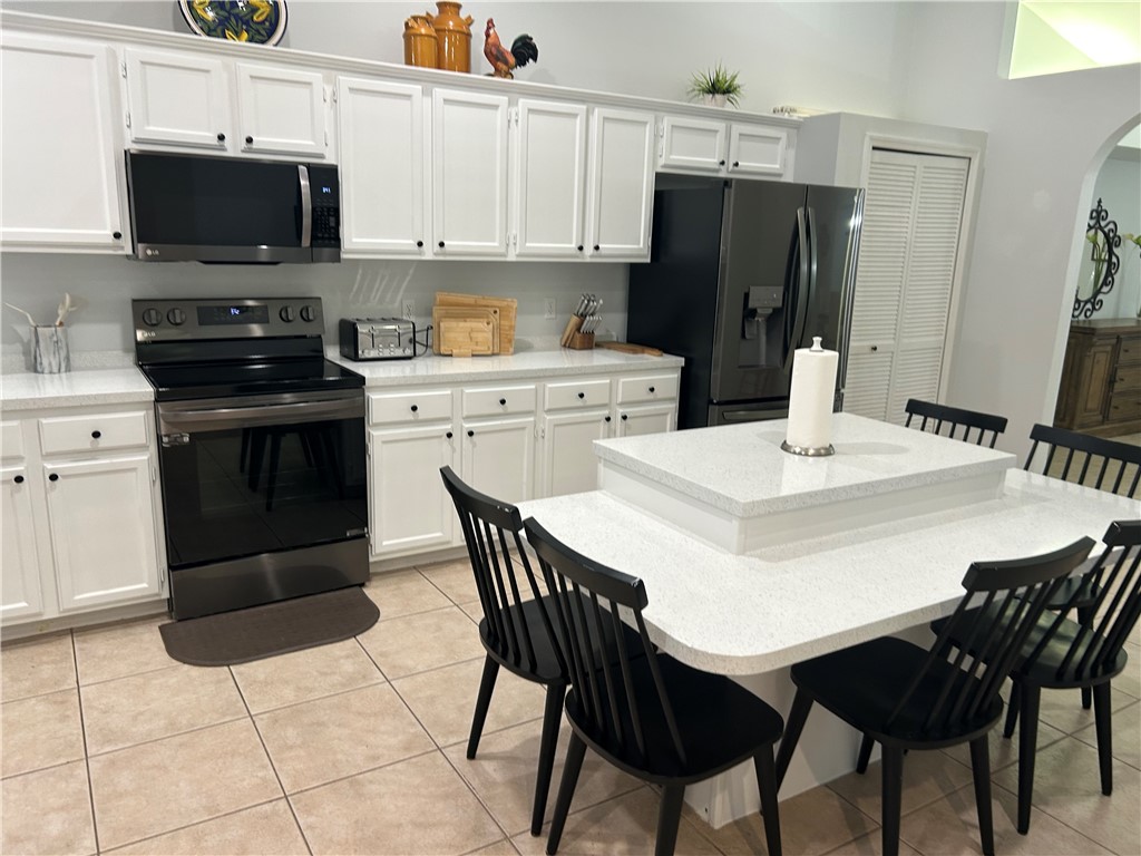 White cabinetry with matte black hardware, integrated black stainless steel appliances, speckled white countertops, and tile flooring