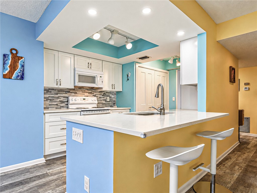 Kitchen featuring white cabinetry, a mosaic tile backsplash, white countertops, a stainless steel sink, and wood-finish flooring