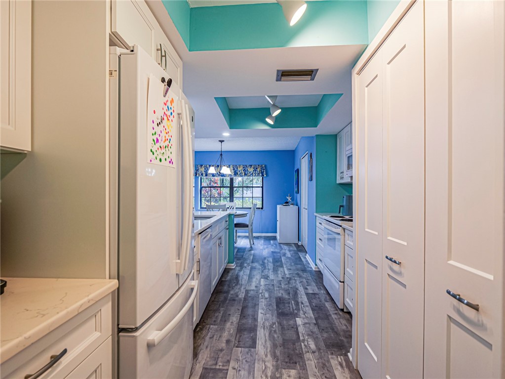 Galley kitchen featuring wood-finish flooring, white cabinetry, integrated appliances, and recessed lighting
