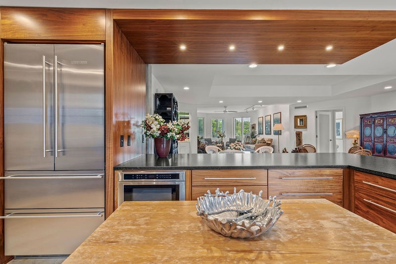 Integrated stainless-steel refrigerator, built-in microwave, wood-finish cabinetry, dark countertop, and recessed ceiling lighting