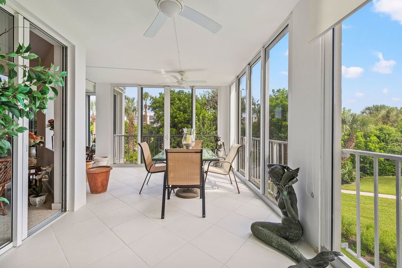 Enclosed balcony featuring expansive windows, white tile flooring, ceiling fans, and sliding glass door access