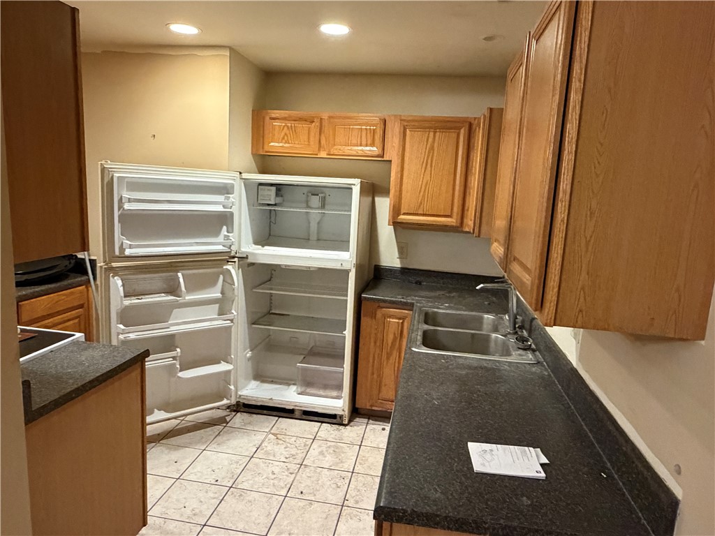 Kitchen featuring wood-finish cabinetry, dark countertops, a double basin stainless steel sink, and tiled flooring