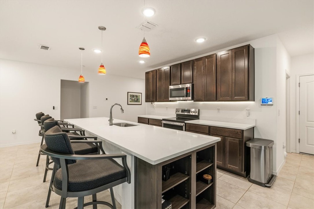 Expansive kitchen island with a built-in sink and seating, dark wood-finish cabinetry, stainless steel appliances, and recessed lighting