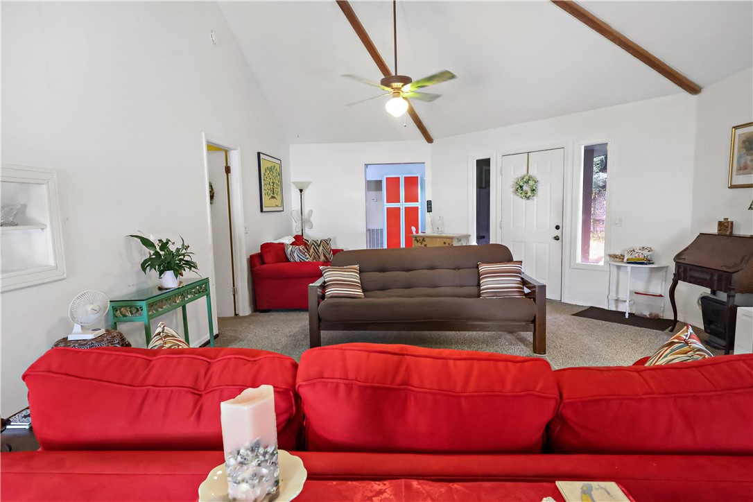 Living area featuring vaulted ceilings with exposed wood beams, a ceiling fan, and carpeted flooring