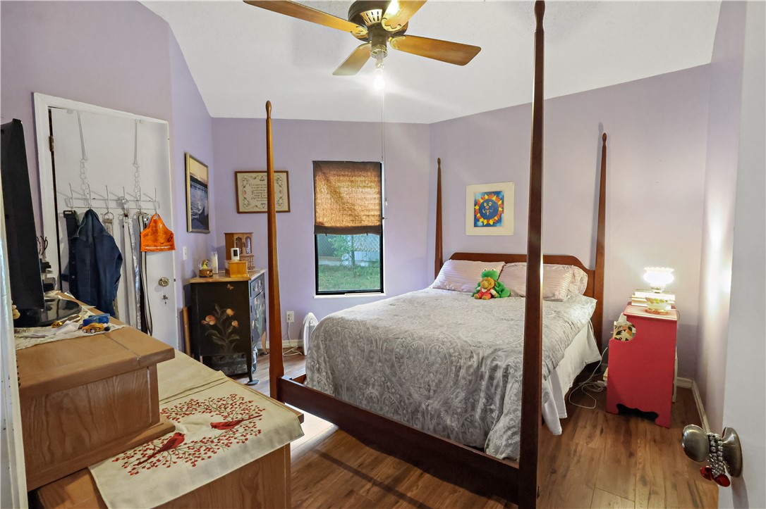 Vaulted ceiling with a ceiling fan, wood-finish flooring, and a window with a woven shade