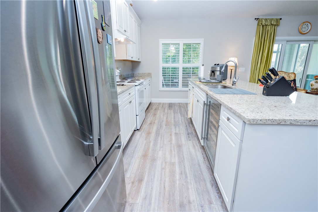 Kitchen featuring white style cabinetry, stone-surface countertops, wood-finish flooring, stainless steel refrigerator, and integrated wine cooler