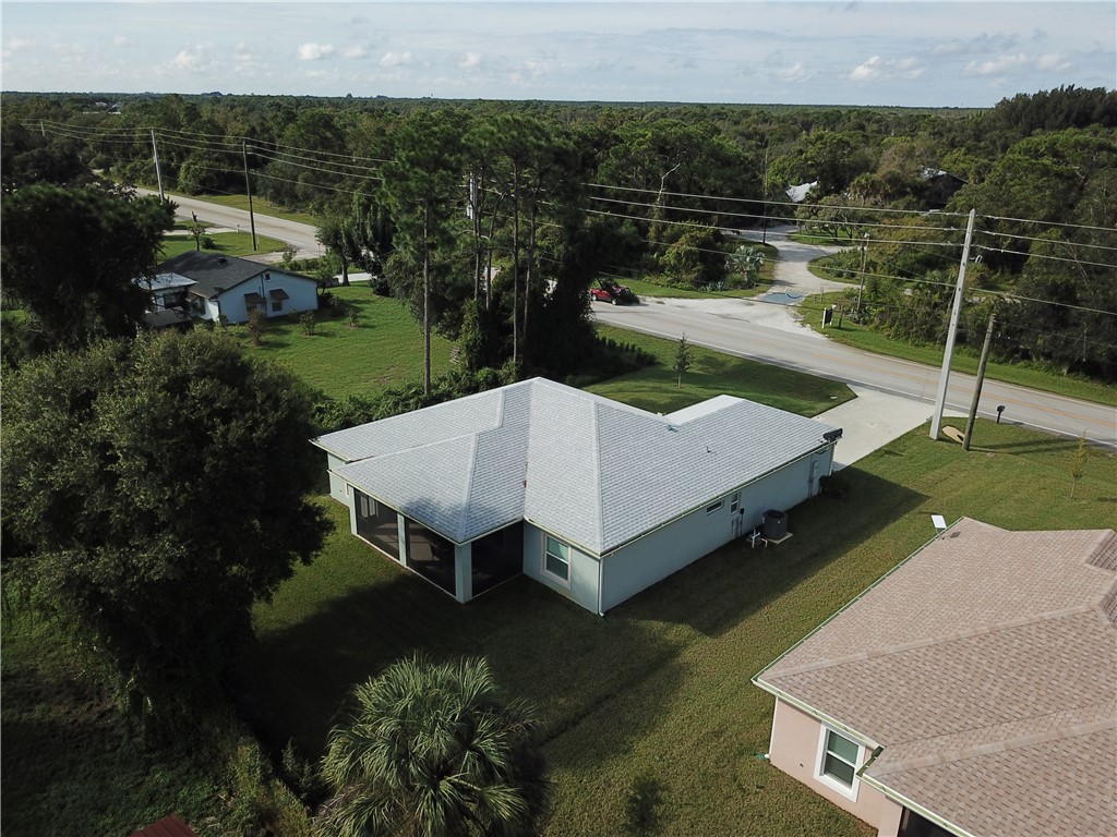 Aerial view of property featuring a hip roof, screened-in rear lanai, concrete driveway, and expansive lawn with mature landscaping