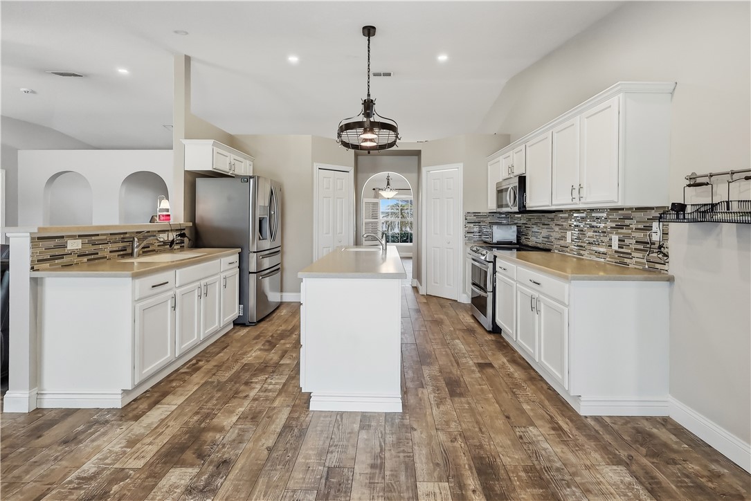 Gourmet kitchen featuring a central island, wood-finish flooring, white cabinetry, stainless steel appliances, and a tiled backsplash