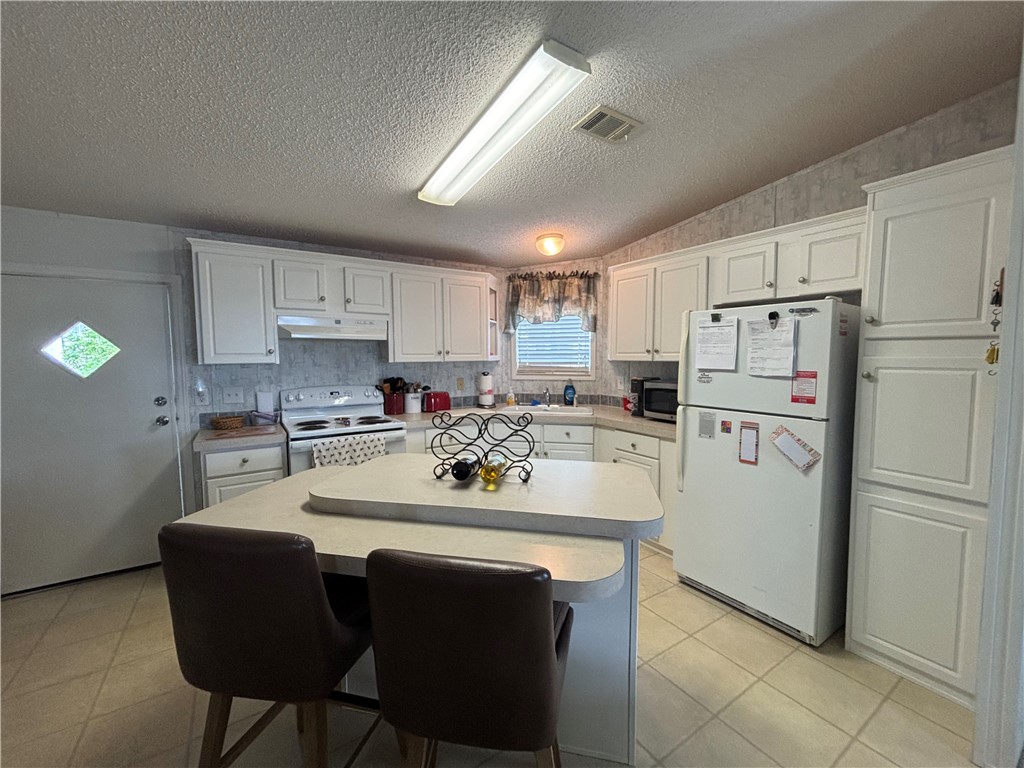 Kitchen featuring white cabinetry, a built-in island with seating, a white electric range, and tiled flooring