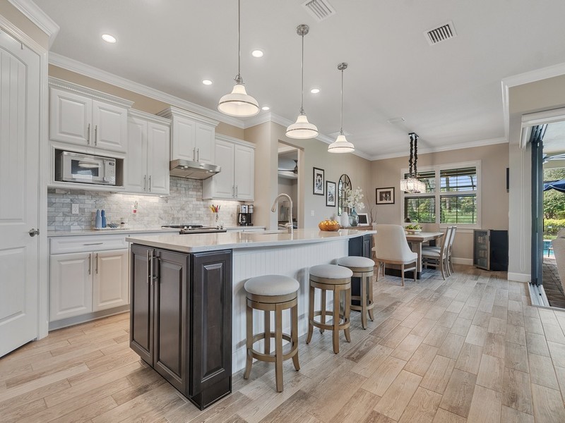 Kitchen featuring white shaker-style cabinetry, a contrasting dark-finish center island, stone-tiled backsplash, pendant lighting, and wood-finish flooring