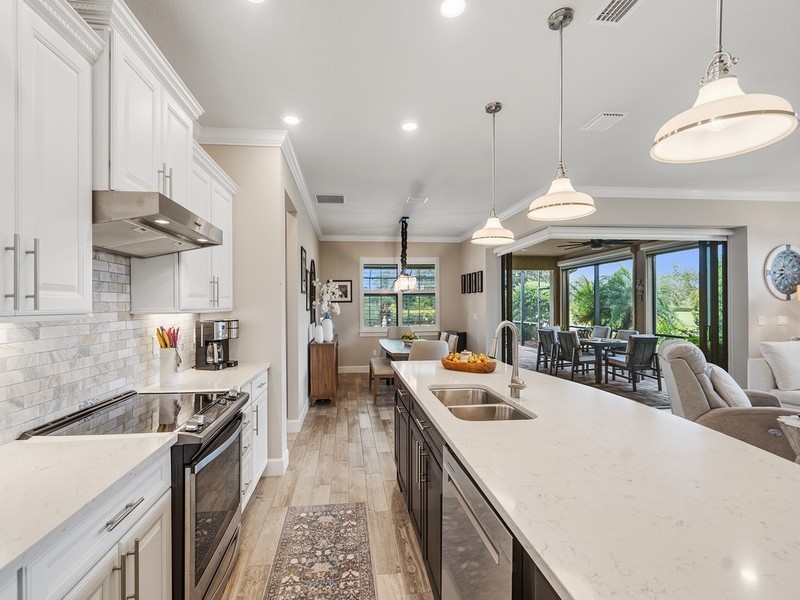 Kitchen featuring wood-finish flooring, white shaker-style cabinetry, a contrasting dark-toned kitchen island with a light-colored countertop, stone-tiled backsplash, and stainless-steel appliances