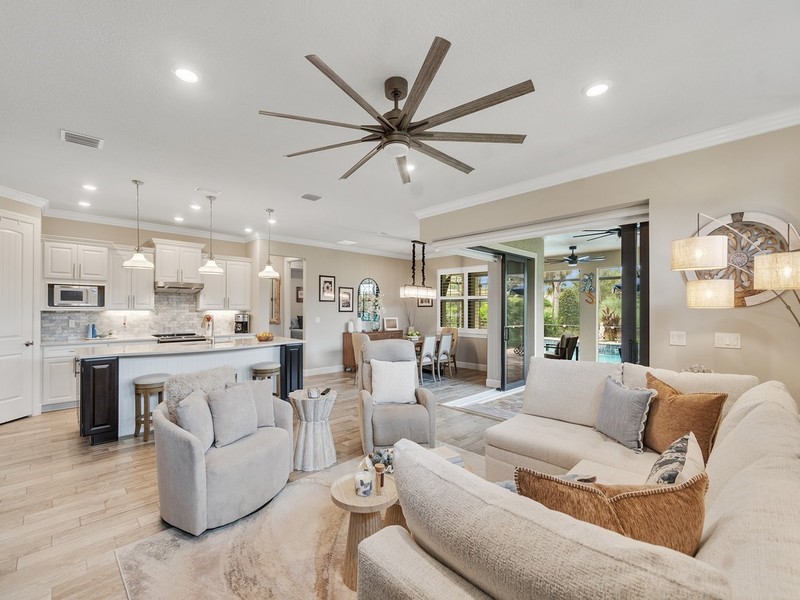Open-concept living space featuring wood-finish flooring, a kitchen island with built-in cabinetry, recessed lighting, a multi-blade ceiling fan, and multi-panel sliding glass doors