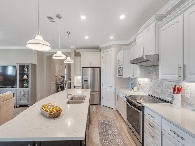 Kitchen featuring an expansive center island with quartz countertops, custom shaker-style cabinetry, a stone-tile backsplash, stainless steel appliances, and pendant lighting