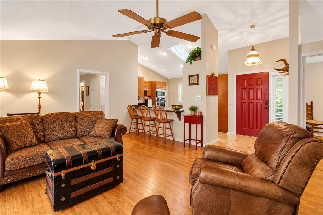 Vaulted ceilings featuring recessed lighting, a skylight, and a ceiling fan, complemented by wood-finish flooring and a distinctive paneled entrance door