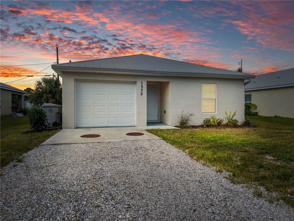 Stucco exterior featuring a hipped roof, attached one-car garage, and gravel driveway