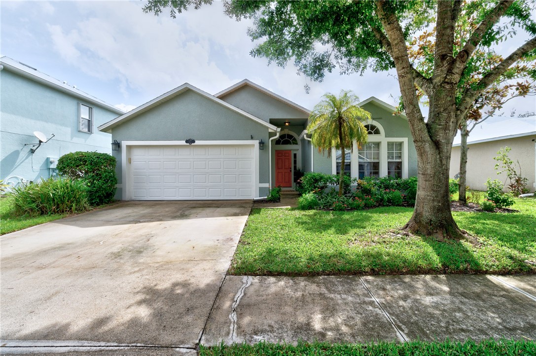 Single-story exterior featuring a stucco facade, attached two-car garage, arched entryway, and mature landscaping