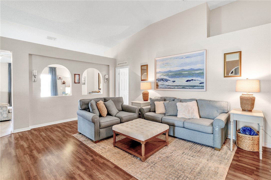 Living area featuring vaulted ceilings, wood-finish flooring, and dual arched wall cutouts with integrated wall sconces